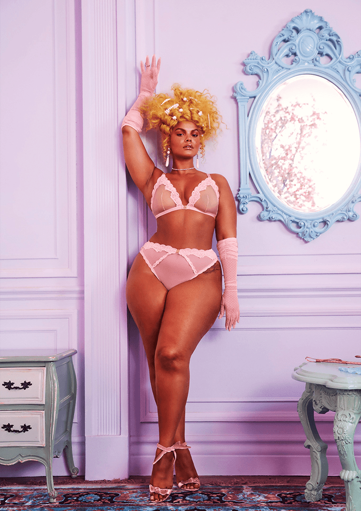 A model wearing pink lingerie leaning against a wall
