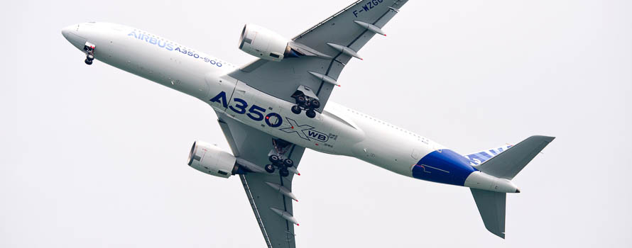 A photograph of the underside of an airborne Airbus A350 aircraft, showing the landing gear deployed.