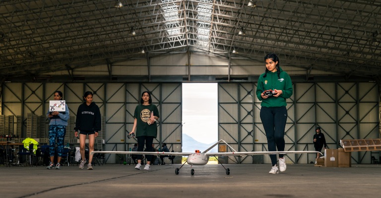 Four students walk towards the small aircraft that they are about to make fly.