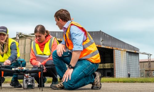 Four students in high-vis crouch down to inspect their drone.