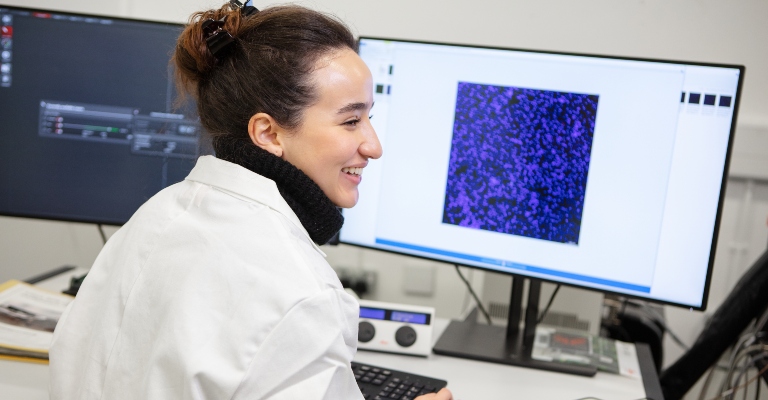 A scientist smiles while working on a desktop computer