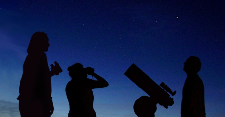 Silhouettes of stargazers looking up into the night sky.