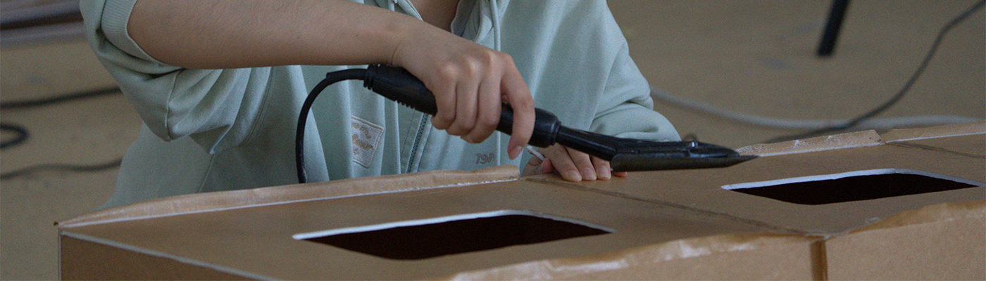 A student is using a glue gun to stitch together foamboard