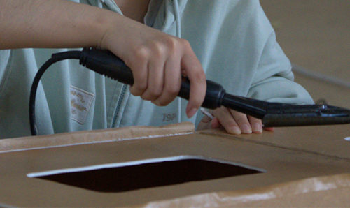 A student is using a glue gun to stitch together foamboard