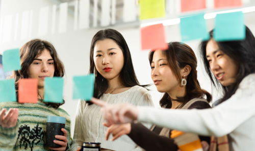 Four students looking at post-it notes on a wall.