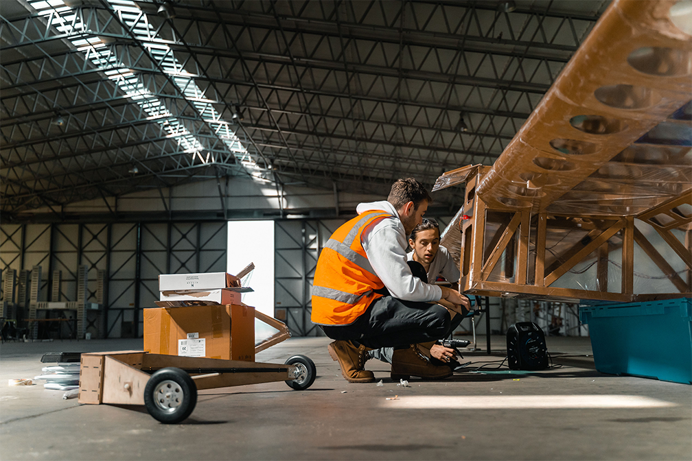 Two individuals working on a giant foamboard aircraft.