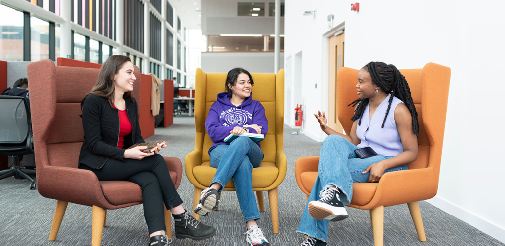 Three students sat in armchairs chatting.