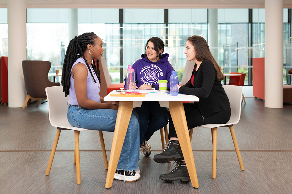 Three students sat at a table chatting.