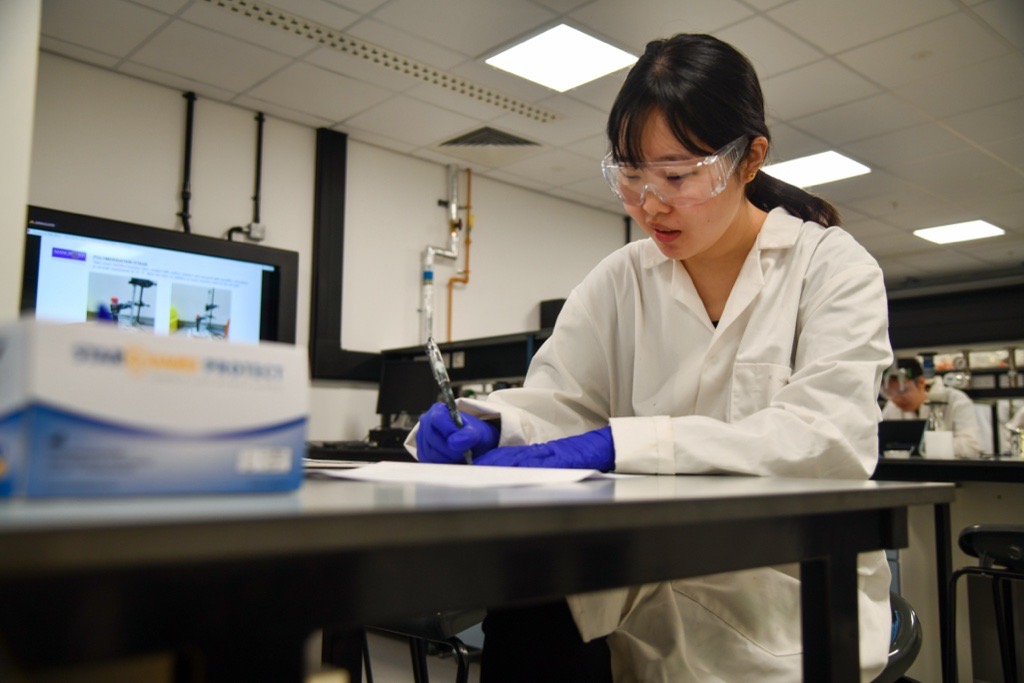 A student wearing a lab coat, goggles and gloves in a laboratory.
