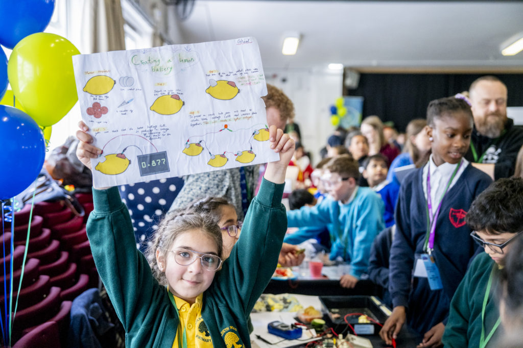 A child holding up a piece of paper with a group of people in the background