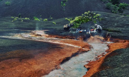 Person squatting next to hot springs on a volcano.