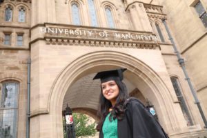 Aiswarya in her graduation cap and gown standing in front of the University of Manchester Whitworth building